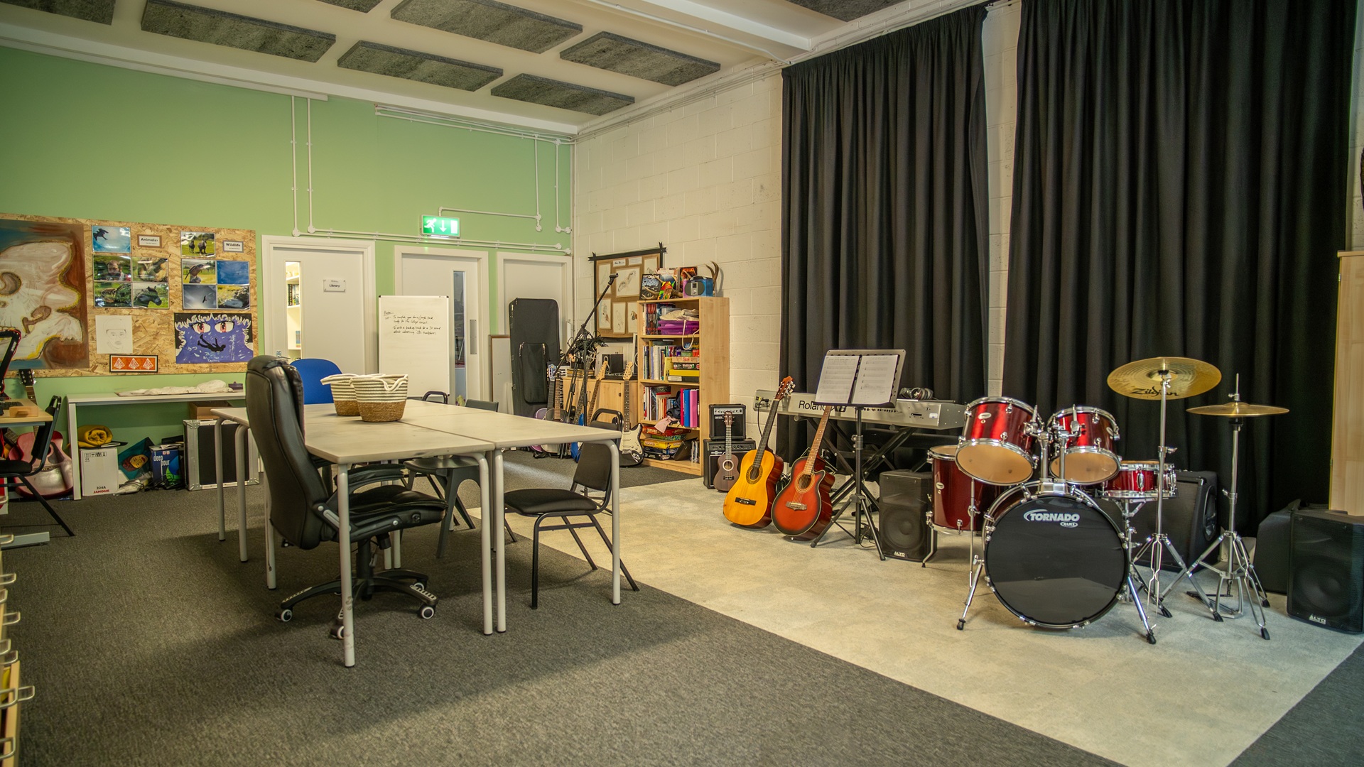 Large room with guitars, drum kit, keyboard and art space with tables
